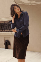 A woman in a navy blue satin button-down shirt and a dark brown suede pencil skirt.