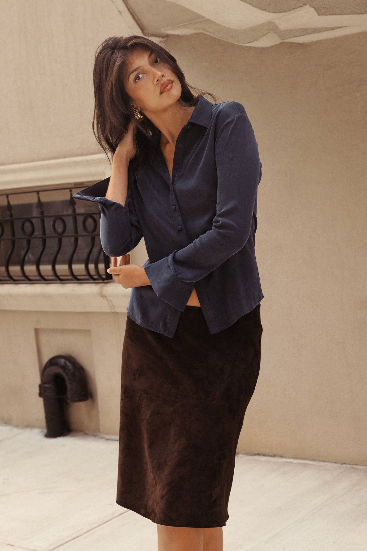 A woman in a navy blue satin button-down shirt and a dark brown suede pencil skirt.