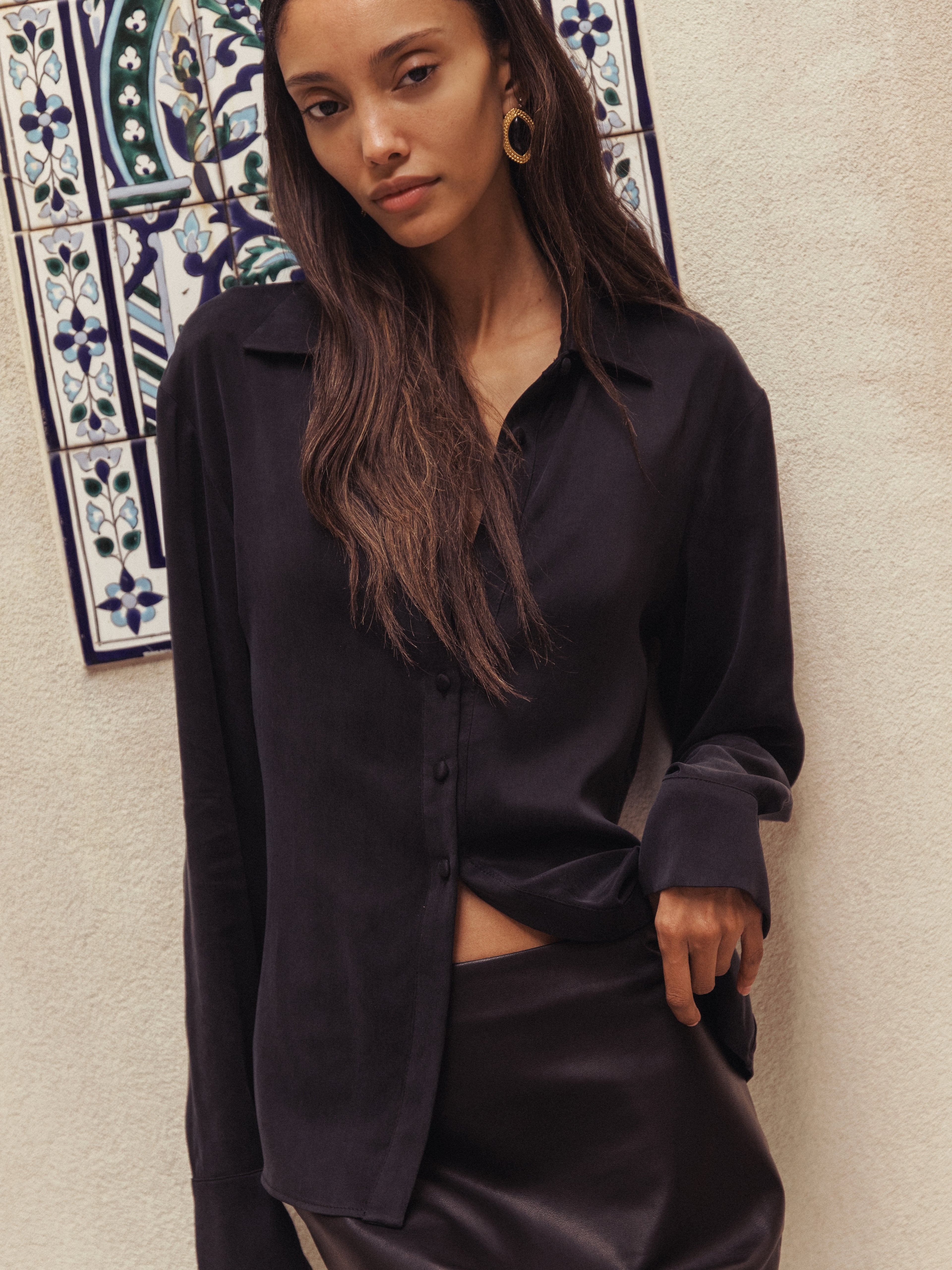 A woman wearing a dark, silky button-up shirt and a leather skirt,.