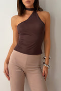 Woman wearing a brown one-shoulder top and beige pants against a plain background