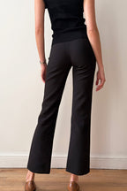 Person wearing black pants and a black top against a plain background