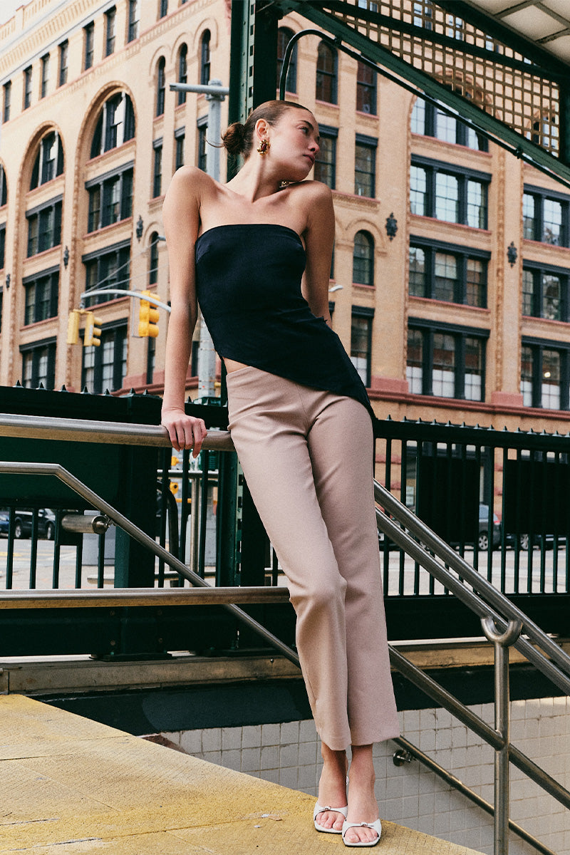 Woman in black top and beige pants standing on a city street with buildings in the background