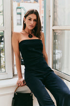 Model in a strapless black top and blue pants sitting by a window.