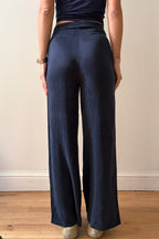 Model wearing navy blue pants standing against a plain wall.