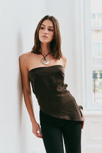 Model wearing a strapless brown top and black pants in an apartment