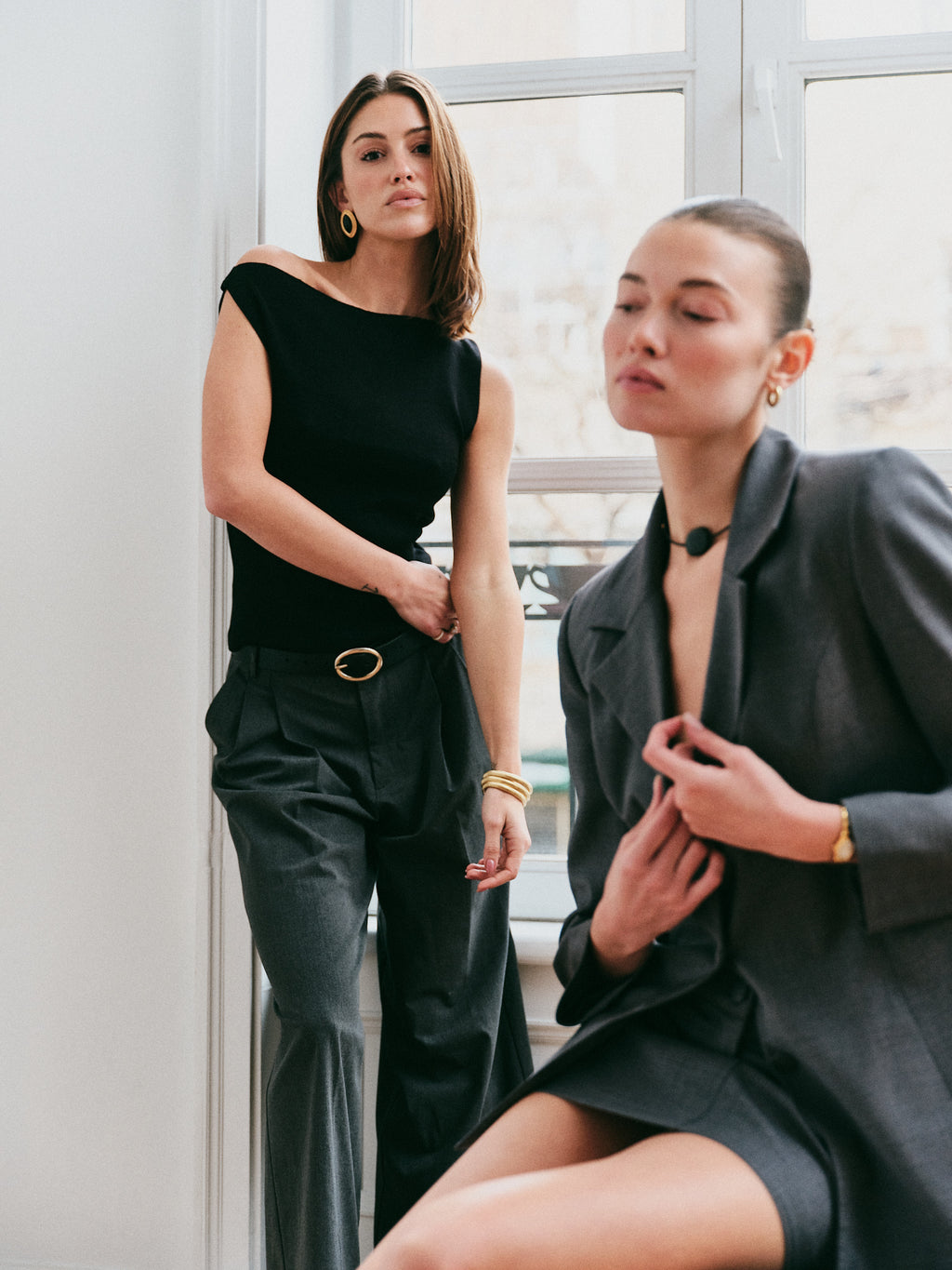 Model wearing the Arue Studios Line Trouser in grey, a tailored wide-leg pleated pant with a relaxed drape and high-rise fit.
