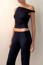 Model  wearing a black off-shoulder top and black pants against a beige background