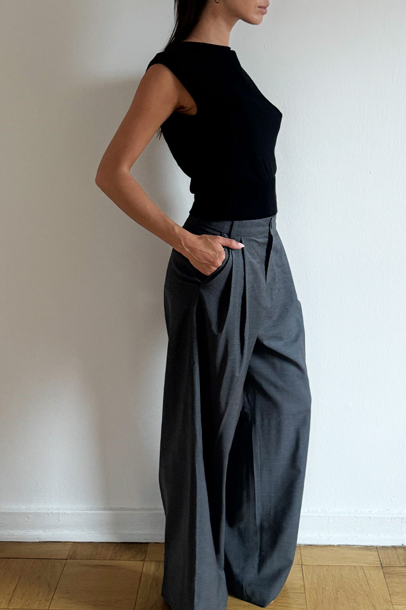 Model wearing the Arue Studios Line Trouser in grey, a tailored wide-leg pleated pant with a relaxed drape and high-rise fit.
