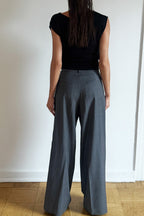 Model wearing the Arue Studios Line Trouser in grey, a tailored wide-leg pleated pant with a relaxed drape and high-rise fit.
