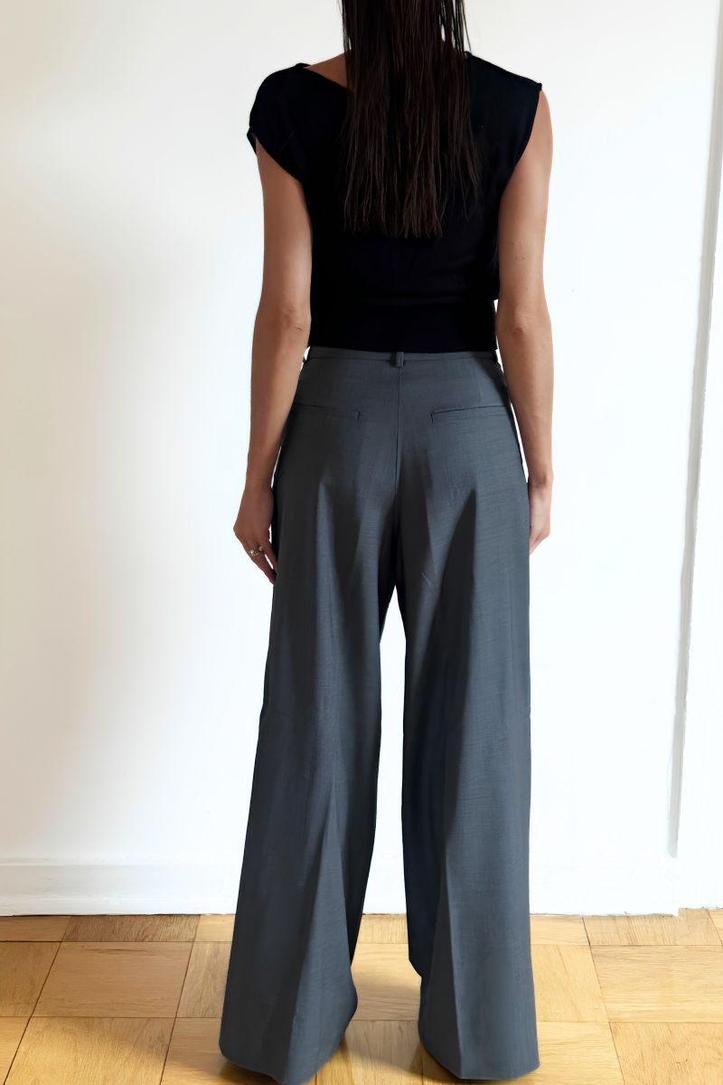 Model wearing the Arue Studios Line Trouser in grey, a tailored wide-leg pleated pant with a relaxed drape and high-rise fit.
