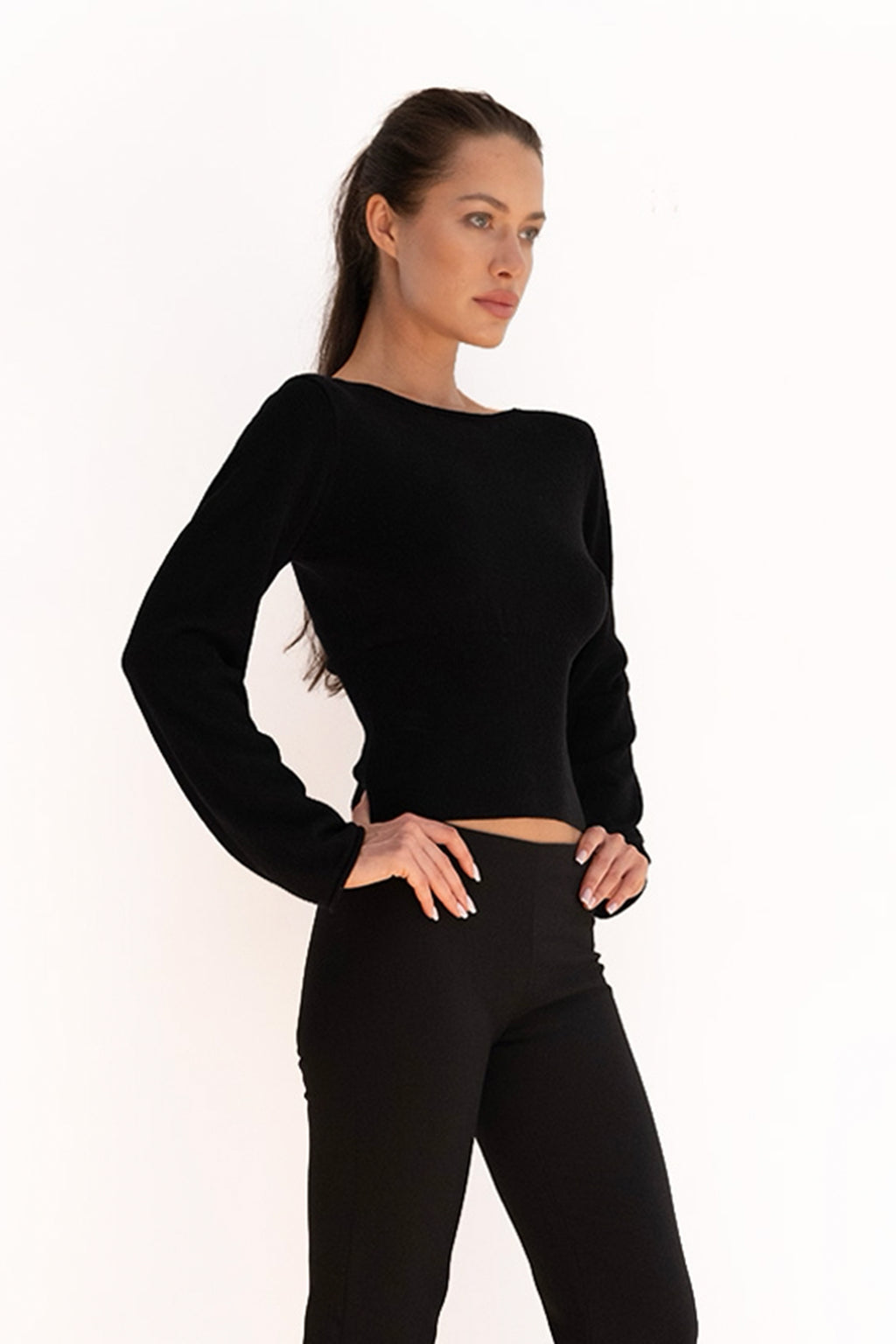 Model wearing the black Mode Knit Top with a boat neckline, long sleeves, and a cinched waist.