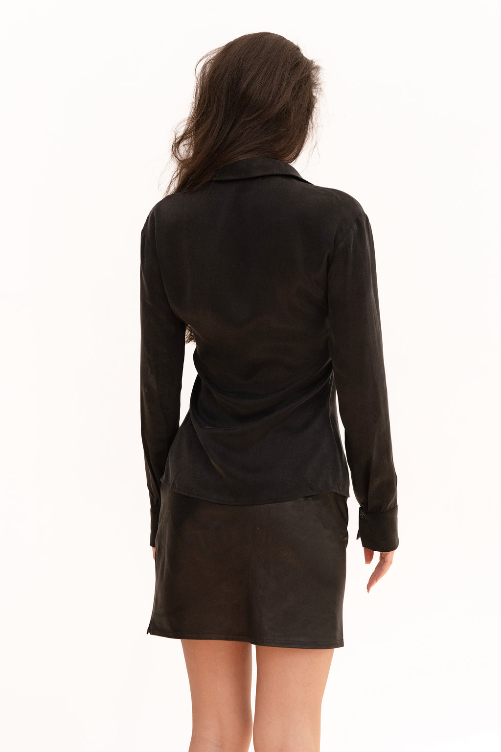 A model wearing a black long-sleeve button-front shirt with a low open neckline and a matching black leather mini skirt, 