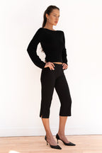 Model wearing black cropped capri trousers with a matching black top and pointed-toe heels