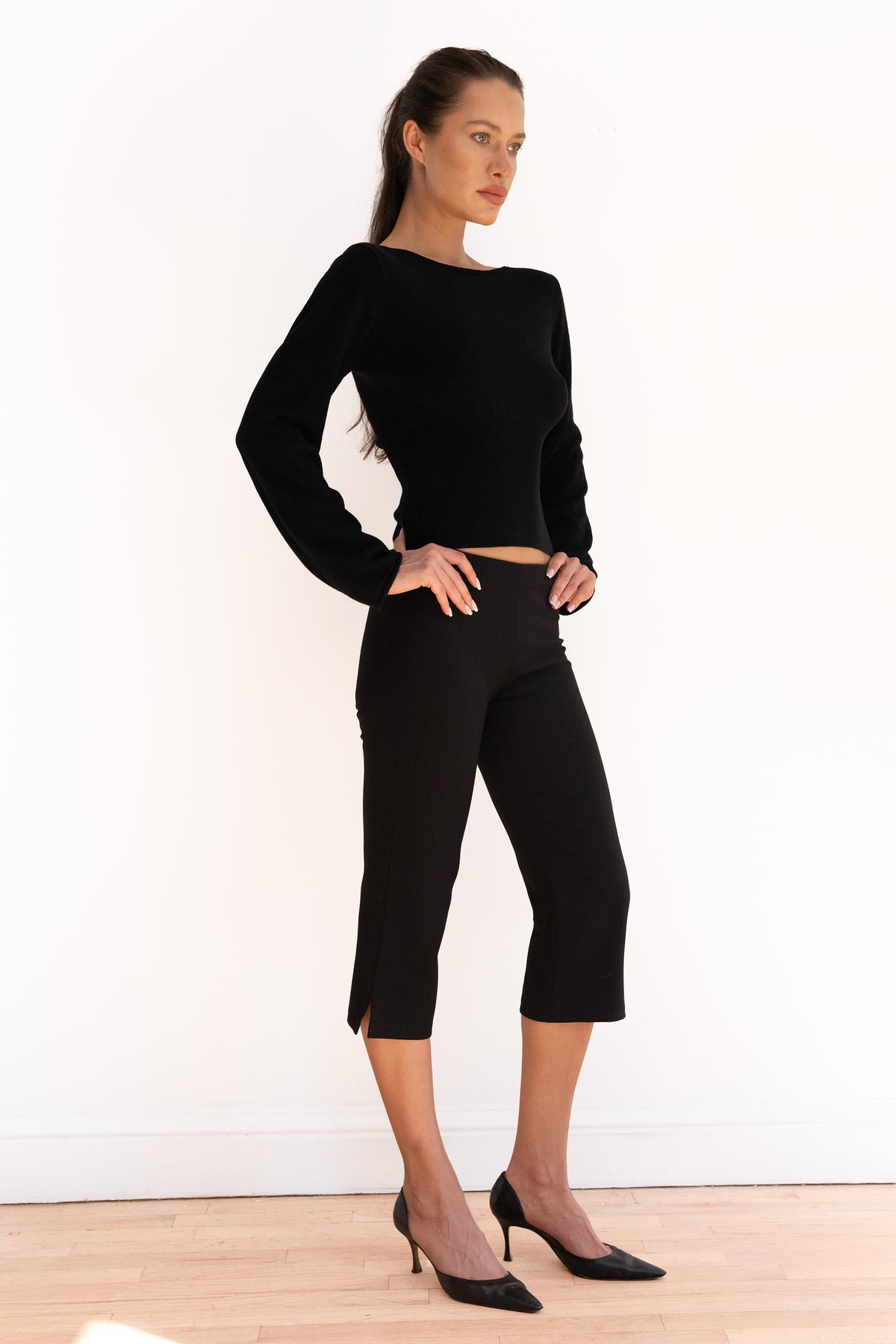 Model wearing black cropped capri trousers with a matching black top and pointed-toe heels