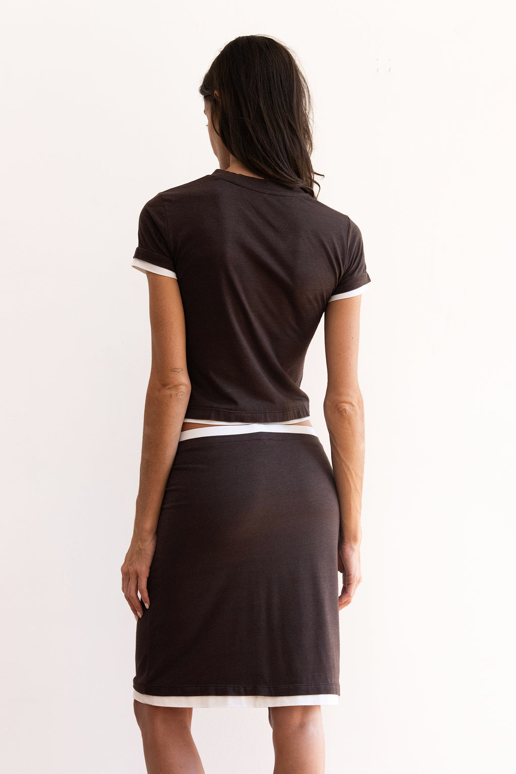 Model wearing the Remi Skirt in espresso brown with ivory contrast waistband and hem, styled low on the waist