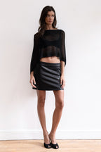 A model wearing a black sheer shawl with a black leather mini skirt and black pointed-toe heels.