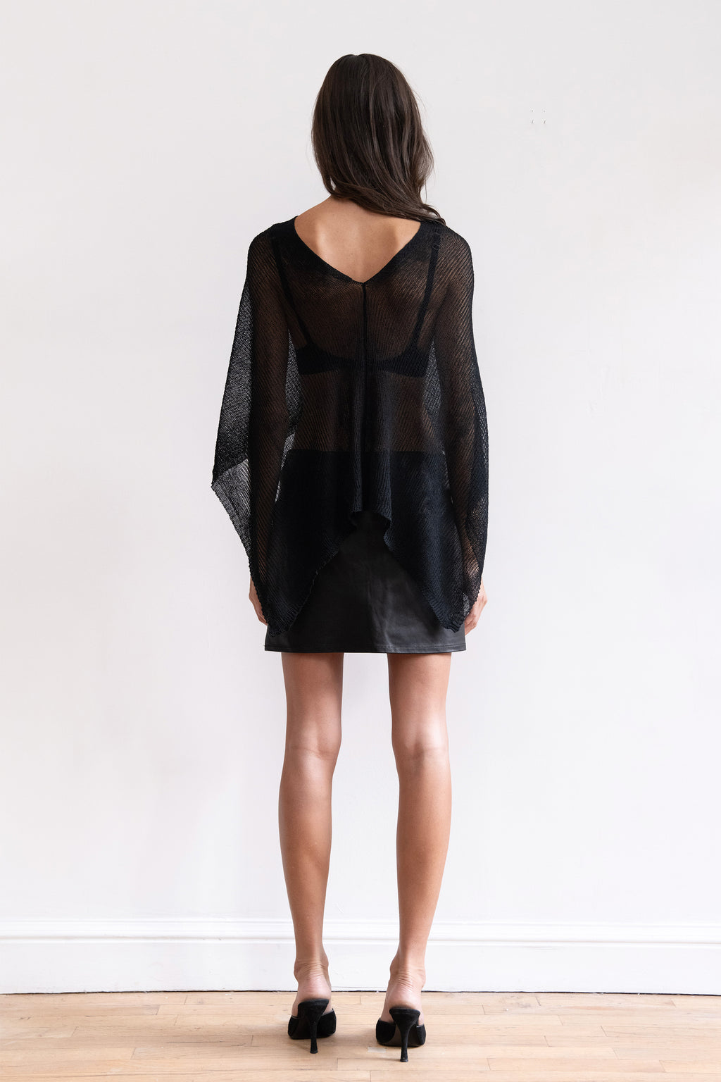 A model wearing a black sheer shawl with a black leather mini skirt and black pointed-toe heels.