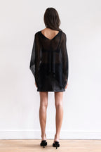 A model wearing a black sheer shawl with a black leather mini skirt and black pointed-toe heels.