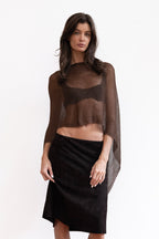 A model wearing a sheer dark brown long-sleeve shawl knit top with a black midi skirt and brown heeled sandals.