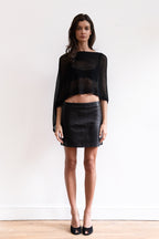 A model wearing a black sheer shawl with a black leather mini skirt and black pointed-toe heels.