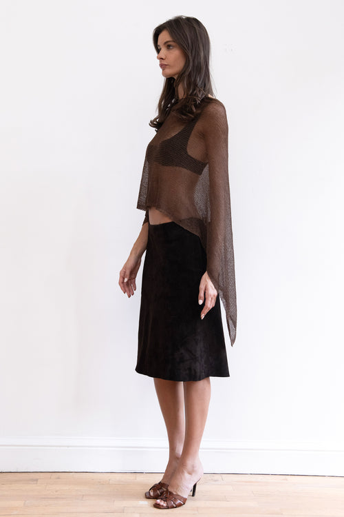 A model wearing a sheer dark brown long-sleeve shawl knit top with a black midi skirt and brown heeled sandals.