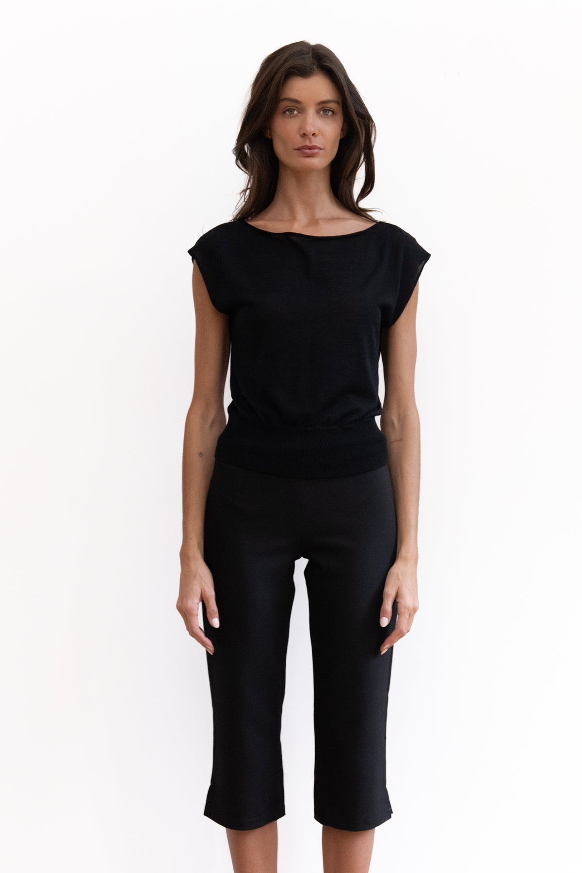 A woman modeling a black short-sleeve top and black cropped pants against a plain white studio background.
