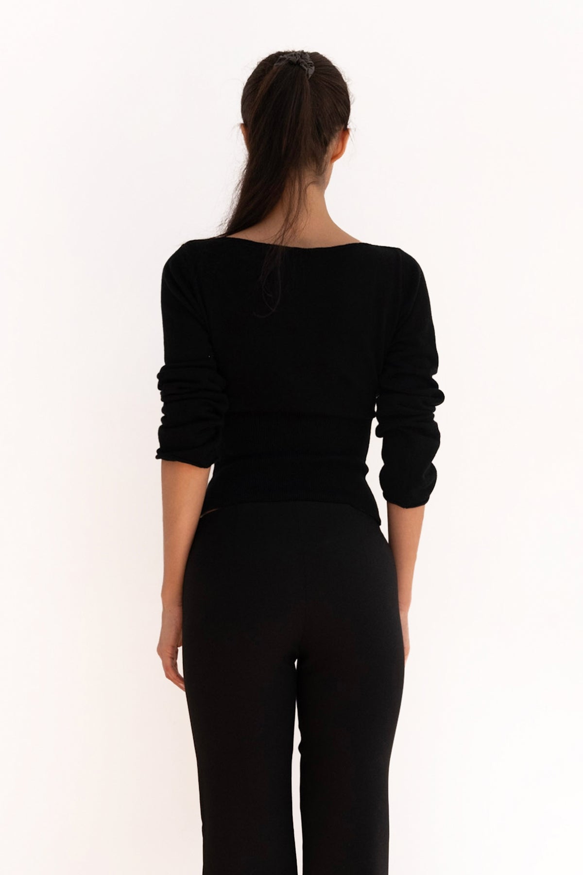 Model wearing the black Mode Knit Top with a boat neckline, long sleeves, and a cinched waist.
