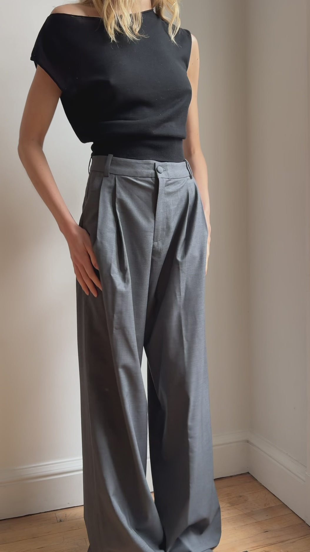 Model wearing the Arue Studios Line Trouser in grey, a tailored wide-leg pleated pant with a relaxed drape and high-rise fit.

