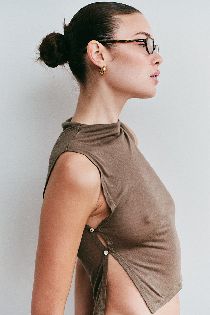 Woman wearing a brown sleeveless top with buttons on a plain background