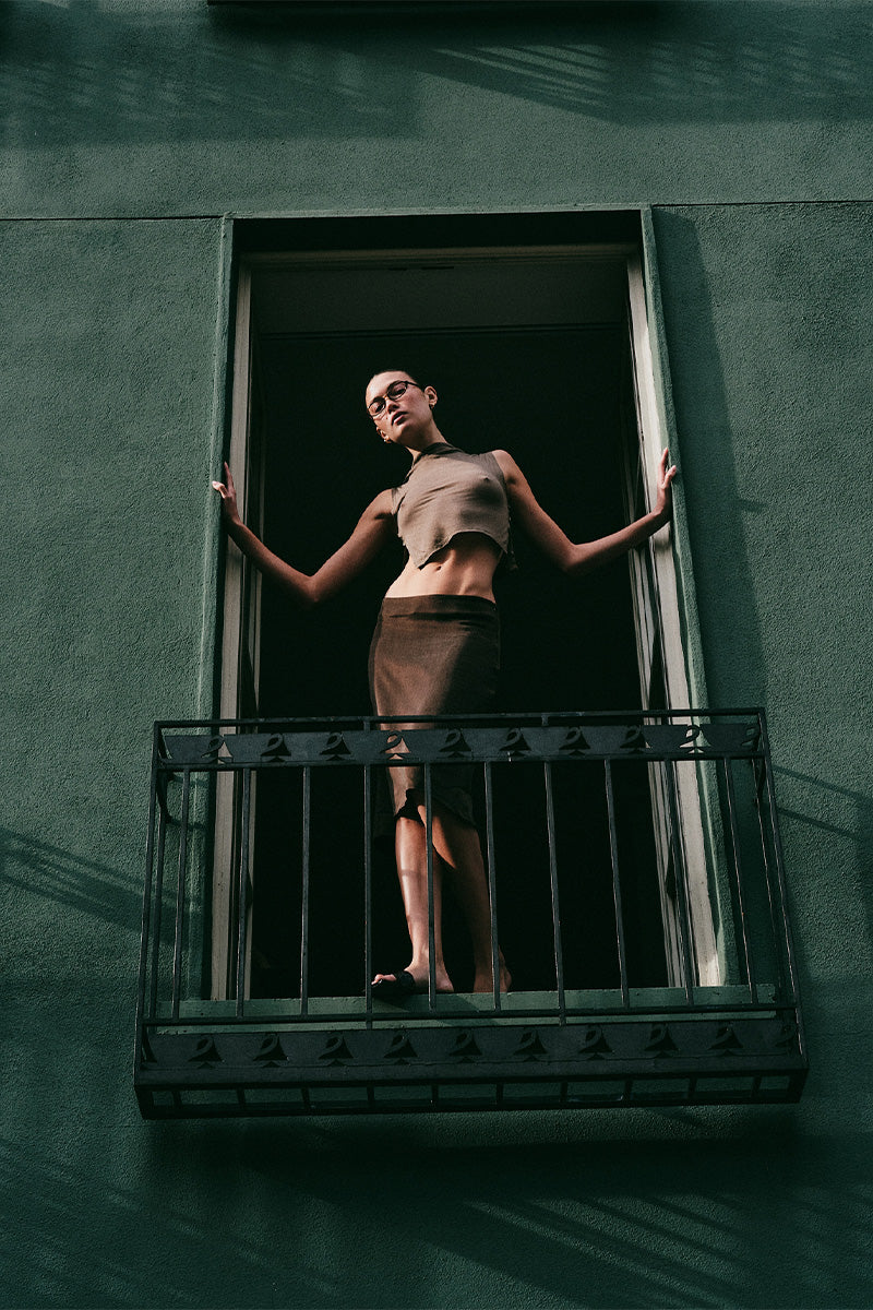Model standing in an open window with a dark green building exterior